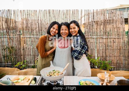 Glückliche südostasiatische Familie, die Spaß beim Lächeln vor der Kamera hat, während sie gemeinsam auf der Terrasse des Hauses thailändisches Rezept zubereitet Stockfoto