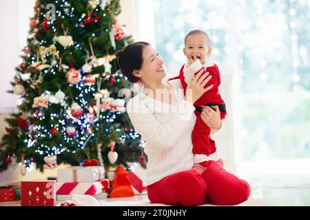 Asiatische Familie mit Kindern am Weihnachtsbaum und Kamin. Mutter und Kinder öffnen Geschenke am Kamin. Baby und Mutter öffnen Geschenke. Winterferien i Stockfoto