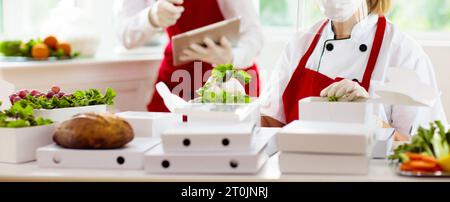 Essen zum Mitnehmen im Restaurant. Das Personal im Cafe kocht zum Mitnehmen. Sicherheit und Hygiene bei der Lieferung von Lebensmitteln nach Hause. Koch mit Salat in Pappbehälter Stockfoto