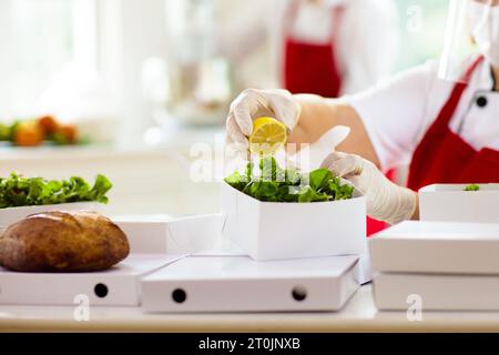 Essen zum Mitnehmen im Restaurant. Das Personal im Cafe kocht zum Mitnehmen. Sicherheit und Hygiene bei der Lieferung von Lebensmitteln nach Hause. Koch mit Salat in Pappbehälter Stockfoto