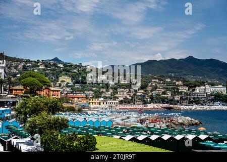 Sonnenanbeter unter Sonnenschirmen am wunderschönen Strand von Santa Margherita Ligure Italien, mit blauem Wasser, historischen Gebäuden und von Bäumen gesäumten Bergen Stockfoto