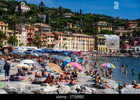 Sonnenanbeter unter Sonnenschirmen am wunderschönen Strand von Santa Margherita Ligure Italien, mit blauem Wasser, historischen Gebäuden und von Bäumen gesäumten Bergen Stockfoto