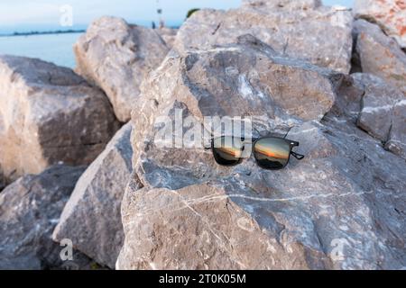 Sonnenuntergang, der in der Reflexion einer Sonnenbrille auf den Felsen eines Leuchtturms am Meer zu sehen ist. Eine Mischung aus warmen Farben wie Orange und Gelb. Stockfoto