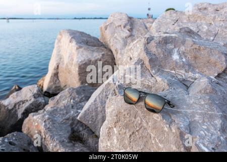 Sonnenuntergang, der in der Reflexion einer Sonnenbrille auf den Felsen eines Leuchtturms am Meer zu sehen ist. Eine Mischung aus warmen Farben wie Orange und Gelb. Stockfoto