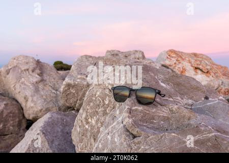 Sonnenuntergang, der in der Reflexion einer Sonnenbrille auf den Felsen eines Leuchtturms am Meer zu sehen ist. Eine Mischung aus warmen Farben wie Orange und Gelb. Stockfoto