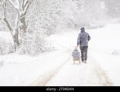 Ein Vater, der sein Kind am schneebedeckten Wintertag bei Schneefall rodelt. Familienurlaub im Winter. Stockfoto