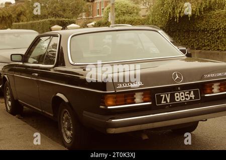 Ein Foto eines schwarzen Mercedes W123, der neben einem Fußweg geparkt ist. Stockfoto