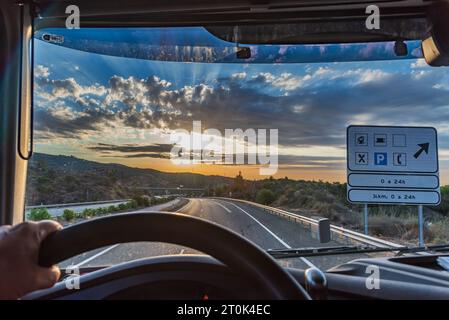 Blick von der Fahrerposition eines Lkws auf eine Autobahn mit einem rund um die Uhr geöffneten Servicebereich, informatives Verkehrsschild. Stockfoto