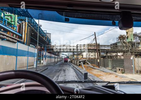 Blick von der Fahrposition eines Lkws auf eine Straße, die zwischen Fabriken mit miteinander verbundenen Rohren verläuft. Stockfoto