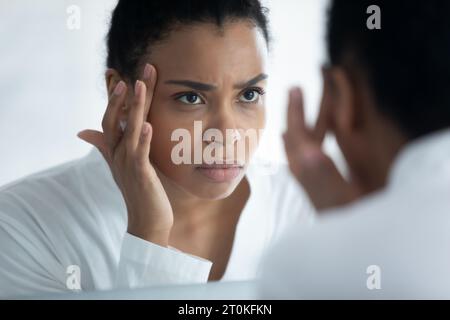 Afroamerikanerin sieht in den Spiegel, besorgt um Gesichtsfalten Stockfoto