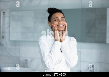 Glückliche birassische Frau berühren gesunde Gesichtshaut im Badezimmer Stockfoto