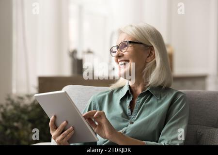 Fröhliche ältere Frau, die auf dem Sofa mit Tablet ruht Stockfoto