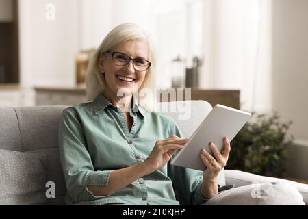 Glückliche, hübsche Seniorin in Brille mit Tablette Stockfoto