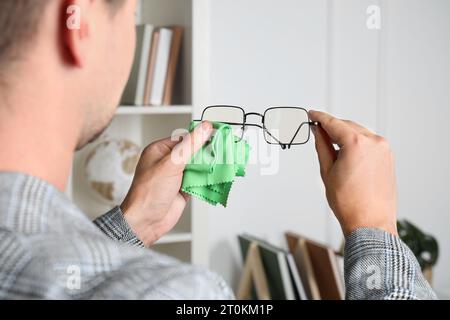 Mann wischt die Brille mit Mikrofasertuch drinnen ab Stockfoto