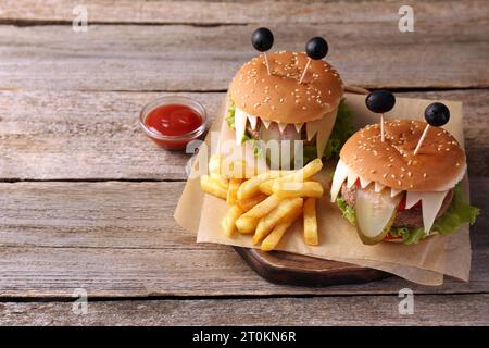 Niedliche Monster Burger serviert mit Pommes frites und Ketchup auf Holztisch, Platz für Text. Halloween Party Essen Stockfoto