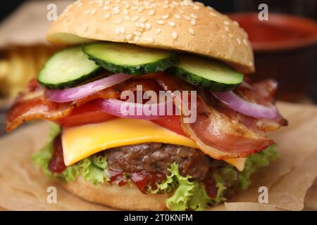 Leckerer Burger mit Speck, Gemüse und Patty auf Pergamentpapier, Nahaufnahme Stockfoto