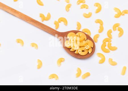 Ungekochte Chifferi Rigati Pasta in Holzlöffel auf weißem Hintergrund. Fett und ungesunde Lebensmittel. Verstreute Klassische Trockene Makkaroni. Italienische Kultur und Küche. Rohe Pasta Stockfoto