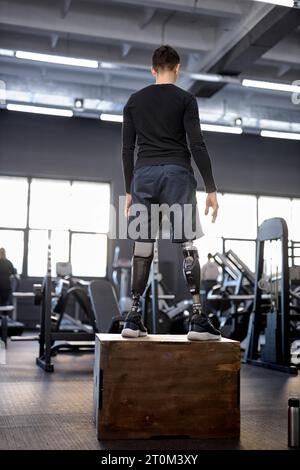 Junger Mann mit künstlichen Beinen, der im Fitnessstudio auf den Boden springt. Kreuzpassung Stockfoto