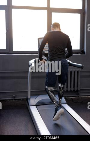 Rückaufnahme eines Mannes mit künstlichen Beinen, der im Fitnessstudio auf Laufbändern läuft, Freizeit, Freizeit, tägliche Routine Wellness. Rehabilitationszentrum, praktizieren. Stockfoto