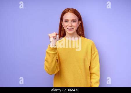 Junge taube stumme Frau mit Gebärdensprache auf blauem Hintergrund, zeigt Buchstabe A, lächelndes Mädchen mit geballter Faust, das auf die Kamerakörpersprache Closeu blickt Stockfoto