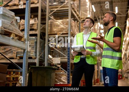 Männer Lagerarbeiter sprechen, Lagerindustrie und Logistikkonzept. Zwei junge Arbeiter in Uniform diskutieren gemeinsam. Das Konzept eines guten Managementsystems Stockfoto