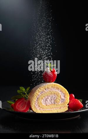 Hausgemachte Erdbeerkekskuchenrolle mit Frischkäse, Schlagsahne und frischen Beeren. Köstlicher Kekskuchen mit Zuckerpulver bestreut. Stockfoto