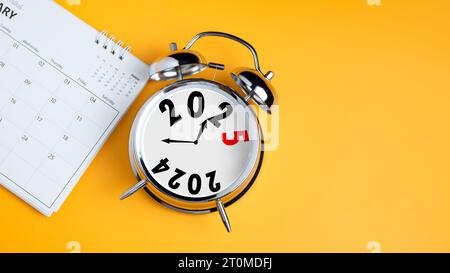 Nahaufnahme von Kalender und Wecker auf gelbem Hintergrund mit Kopierraum. Übergang von 2023 zu 2024, Start-up-Plan für Unternehmen, Countdown Start Stockfoto