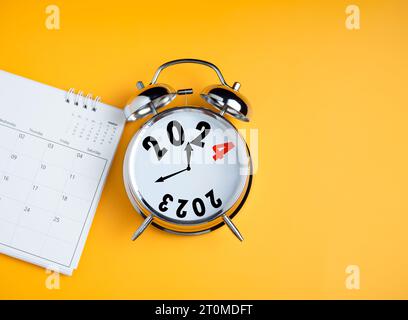 Nahaufnahme von Kalender und Wecker auf gelbem Hintergrund mit Kopierraum. Übergang von 2023 zu 2024, Start-up-Plan für Unternehmen, Countdown Start Stockfoto
