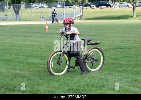 Ein junger chassidischer Junge mit langem Peyot hält während Sukkos auf seinem Fahrrad an. Im Weldler Park in Monsey, einer religiösen jüdischen Gemeinde im Rockkland County, NY. Stockfoto