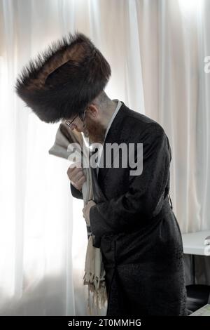 Auf Sukkos faltet ein orthodoxer jüdischer Mann, der einen Schtreimel-Pelzhut trägt, seine tallis am Ende der Morgengottesdienste. In Monsey, Rockland County, New. Stockfoto