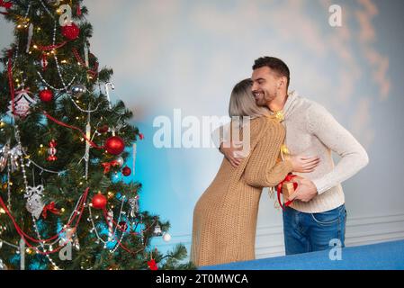 Liebevolles Paar in der Nähe des Weihnachtsbaums. Weihnachts- und Neujahrskonzept. Der Kerl und das Mädchen tauschen Silvestergeschenke in der Nähe des Neujahrsbaums aus. Stockfoto