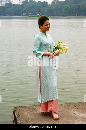 Hanoi, Vietnam. Eine junge Frau, die einen Ao Dai am Lake Hoan Kiem trägt. Stockfoto