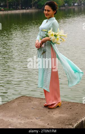 Hanoi, Vietnam. Eine junge Frau, die einen Ao Dai am Lake Hoan Kiem trägt. Stockfoto