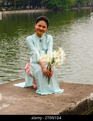 Hanoi, Vietnam. Eine junge Frau, die einen Ao Dai am Lake Hoan Kiem trägt. Stockfoto