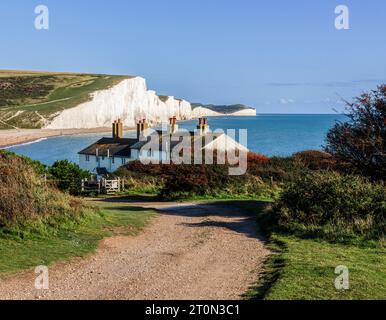 Blick auf die Kreidefelsen der Sieben Sisters und Cottages der Küstenwache von Seaford Head über Cuckmere Haven, die an einem sonnigen Tag mit blauem Himmel nach Osten schauen Stockfoto