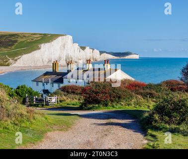 Blick auf die Kreidefelsen der Sieben Sisters und Cottages der Küstenwache von Seaford Head über Cuckmere Haven, die an einem sonnigen Tag mit blauem Himmel nach Osten schauen Stockfoto