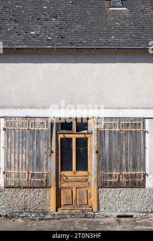 Alte verwitterte, halb verfallene und gebrochene gelb lackierte Holztür mit Seitenfenstern und alten Holzläden davor Stockfoto