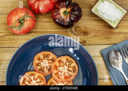 Ein blauer Teller mit Tomatenscheiben auf Holzdielen Stockfoto