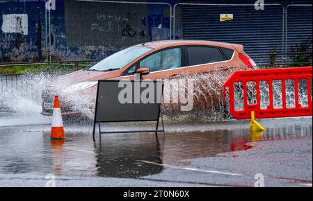 Dundee, Tayside, Schottland, Großbritannien. Oktober 2023. Wetter in Großbritannien: Die Überschwemmungen auf der MacAlpine Road in Ardler Village sind das Ergebnis von nächtlichen sintflutartigen Regenfällen in Dundee. Regen hat die Reise in Dundee beeinflusst und einige Busse aufgrund überfluteter Straßen gezwungen, umzuleiten. Autofahrer werden durch überflutete Straßen gefahren, wodurch Wasser außergewöhnlich hoch spritzt. Quelle: Dundee Photographics/Alamy Live News Stockfoto