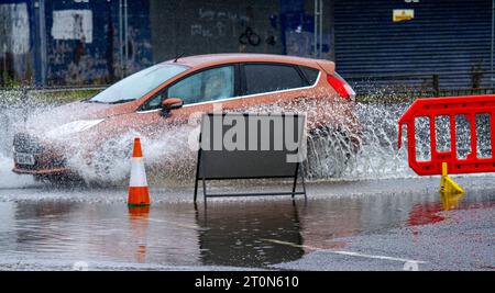 Dundee, Tayside, Schottland, Großbritannien. Oktober 2023. Wetter in Großbritannien: Die Überschwemmungen auf der MacAlpine Road in Ardler Village sind das Ergebnis von nächtlichen sintflutartigen Regenfällen in Dundee. Regen hat die Reise in Dundee beeinflusst und einige Busse aufgrund überfluteter Straßen gezwungen, umzuleiten. Autofahrer werden durch überflutete Straßen gefahren, wodurch Wasser außergewöhnlich hoch spritzt. Quelle: Dundee Photographics/Alamy Live News Stockfoto