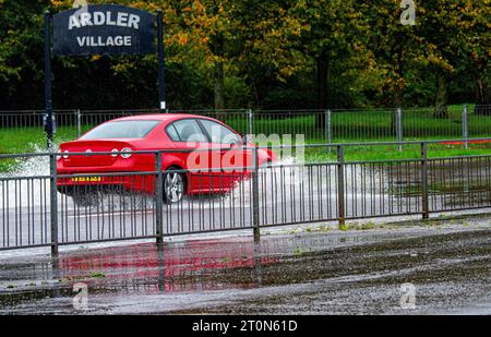 Dundee, Tayside, Schottland, Großbritannien. Oktober 2023. Wetter in Großbritannien: Die Überschwemmungen auf der MacAlpine Road in Ardler Village sind das Ergebnis von nächtlichen sintflutartigen Regenfällen in Dundee. Regen hat die Reise in Dundee beeinflusst und einige Busse aufgrund überfluteter Straßen gezwungen, umzuleiten. Autofahrer werden durch überflutete Straßen gefahren, wodurch Wasser außergewöhnlich hoch spritzt. Quelle: Dundee Photographics/Alamy Live News Stockfoto