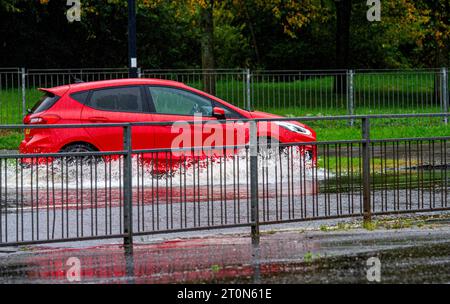 Dundee, Tayside, Schottland, Großbritannien. Oktober 2023. Wetter in Großbritannien: Die Überschwemmungen auf der MacAlpine Road in Ardler Village sind das Ergebnis von nächtlichen sintflutartigen Regenfällen in Dundee. Regen hat die Reise in Dundee beeinflusst und einige Busse aufgrund überfluteter Straßen gezwungen, umzuleiten. Autofahrer werden durch überflutete Straßen gefahren, wodurch Wasser außergewöhnlich hoch spritzt. Quelle: Dundee Photographics/Alamy Live News Stockfoto