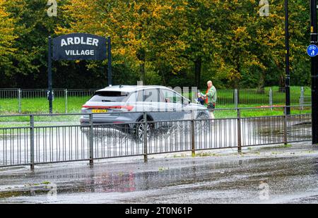 Dundee, Tayside, Schottland, Großbritannien. Oktober 2023. Wetter in Großbritannien: Die Überschwemmungen auf der MacAlpine Road in Ardler Village sind das Ergebnis von nächtlichen sintflutartigen Regenfällen in Dundee. Regen hat die Reise in Dundee beeinflusst und einige Busse aufgrund überfluteter Straßen gezwungen, umzuleiten. Autofahrer werden durch überflutete Straßen gefahren, wodurch Wasser außergewöhnlich hoch spritzt. Quelle: Dundee Photographics/Alamy Live News Stockfoto