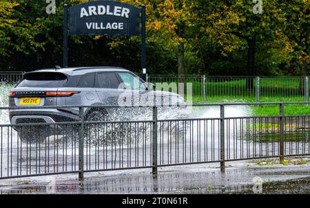 Dundee, Tayside, Schottland, Großbritannien. Oktober 2023. Wetter in Großbritannien: Die Überschwemmungen auf der MacAlpine Road in Ardler Village sind das Ergebnis von nächtlichen sintflutartigen Regenfällen in Dundee. Regen hat die Reise in Dundee beeinflusst und einige Busse aufgrund überfluteter Straßen gezwungen, umzuleiten. Autofahrer werden durch überflutete Straßen gefahren, wodurch Wasser außergewöhnlich hoch spritzt. Quelle: Dundee Photographics/Alamy Live News Stockfoto