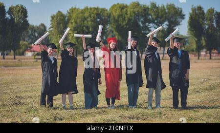 Junge Absolventen posieren und winken Diplome in den Händen auf der Straße. Stockfoto
