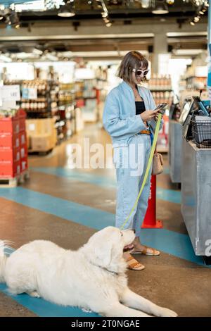 Eine Frau mit ihrem süßen weißen Hund besucht einen Supermarkt Stockfoto