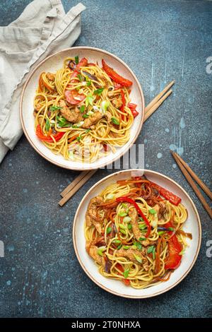 Zwei Schüsseln mit Chow mein oder Lo mein, traditionellen chinesischen Pfannennudeln mit Fleisch und Gemüse, serviert mit Essstäbchen von oben auf rustikalem Blau Stockfoto