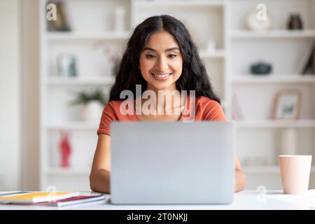 Positive junge hindu-Dame, die von zu Hause aus am Laptop arbeitet Stockfoto