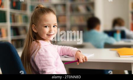 Fröhliches europäisches Schulmädchen an der Rezeption, das sich mit einem Lächeln zurückdreht Stockfoto