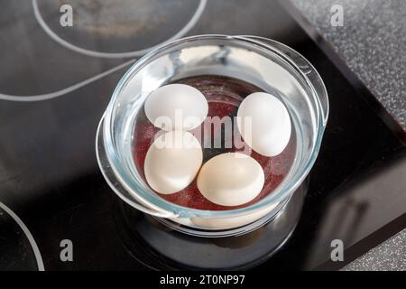 Eier im Wasser im Glastopf auf dem Elektroherd. Kochen gekochter Eier Stockfoto